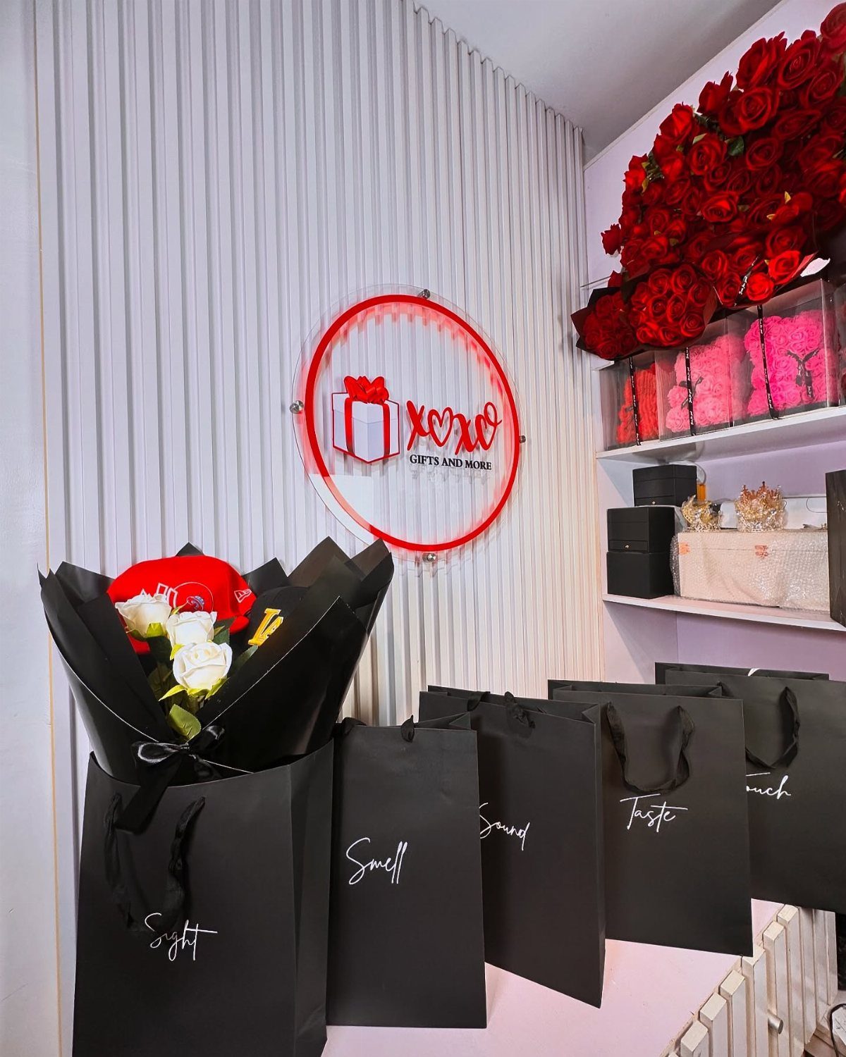 Five black gift bags labeled with the five senses next to red roses.