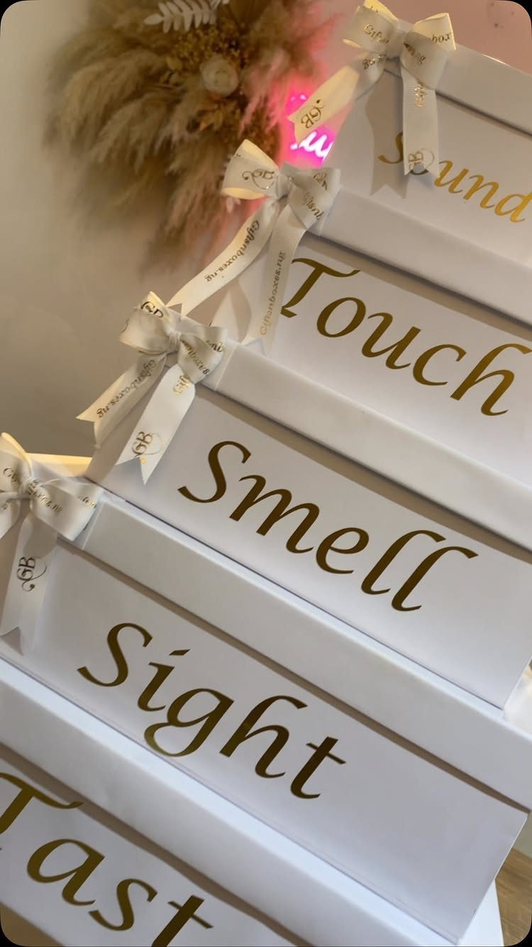 Stacked white gift boxes with gold text labeling the five human senses.