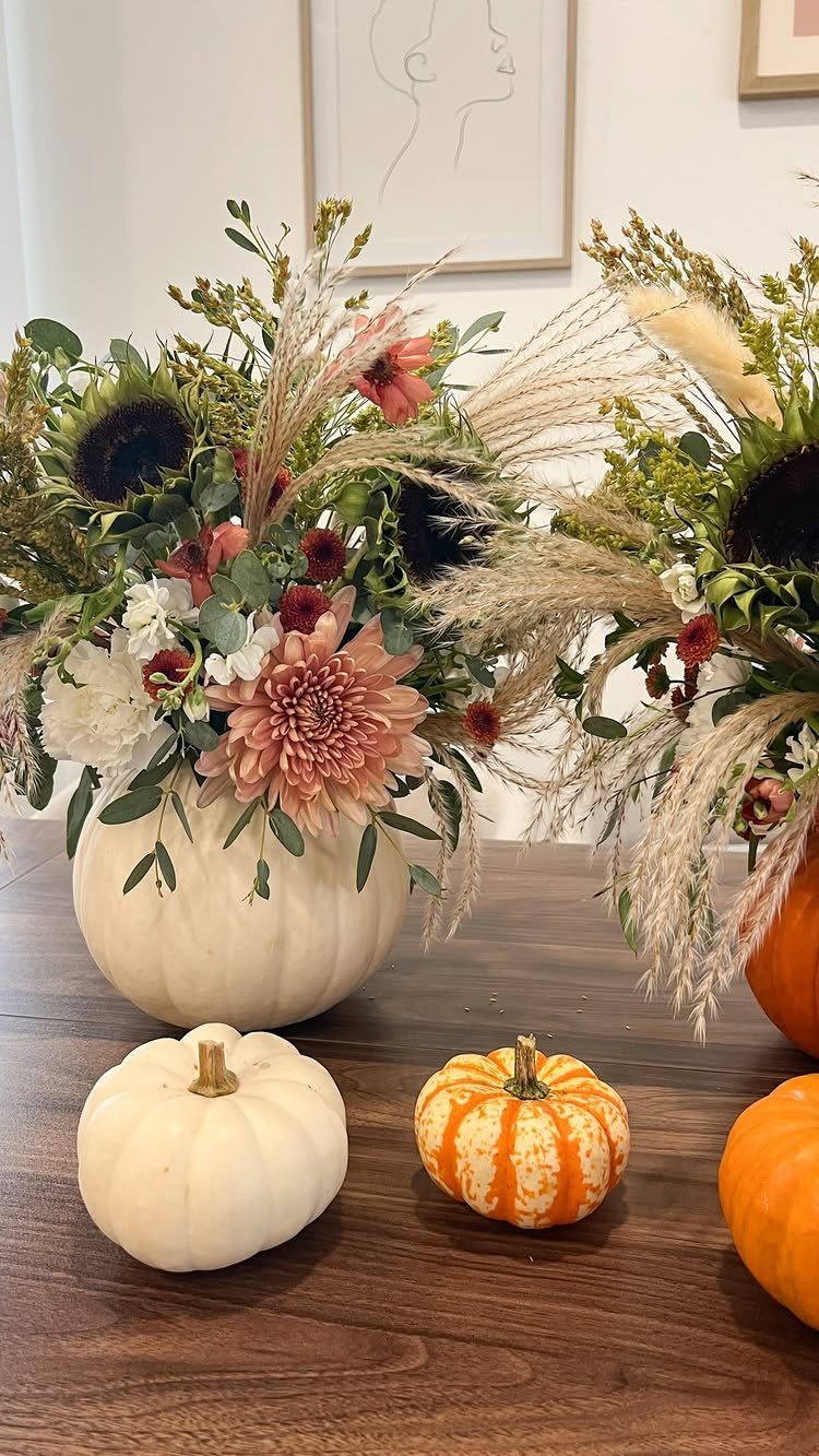 Floral arrangements in pumpkin vases with sunflowers and pampas grass on wooden table