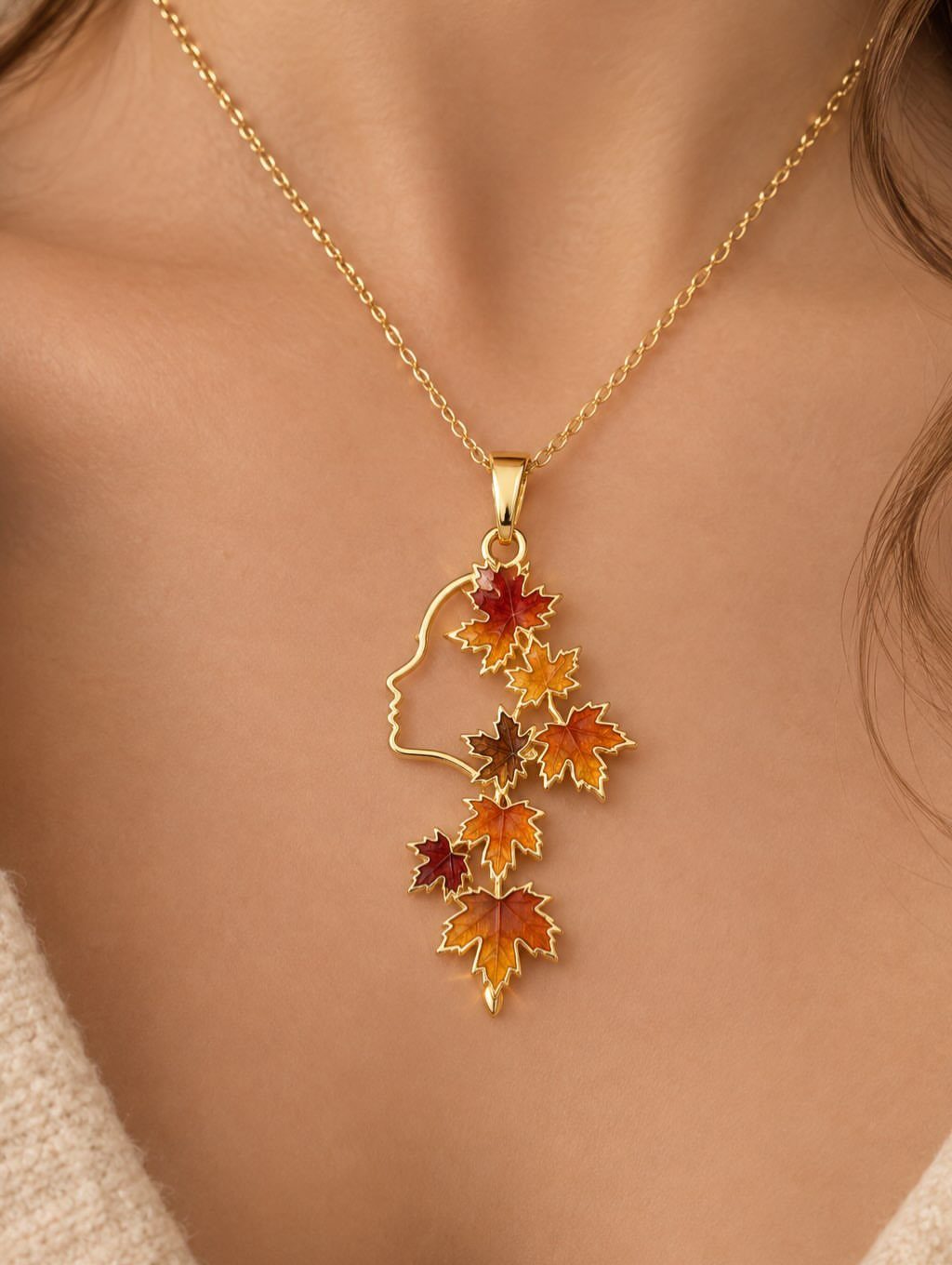 Gold necklace with a pendant featuring a woman's profile and colorful autumn leaves.