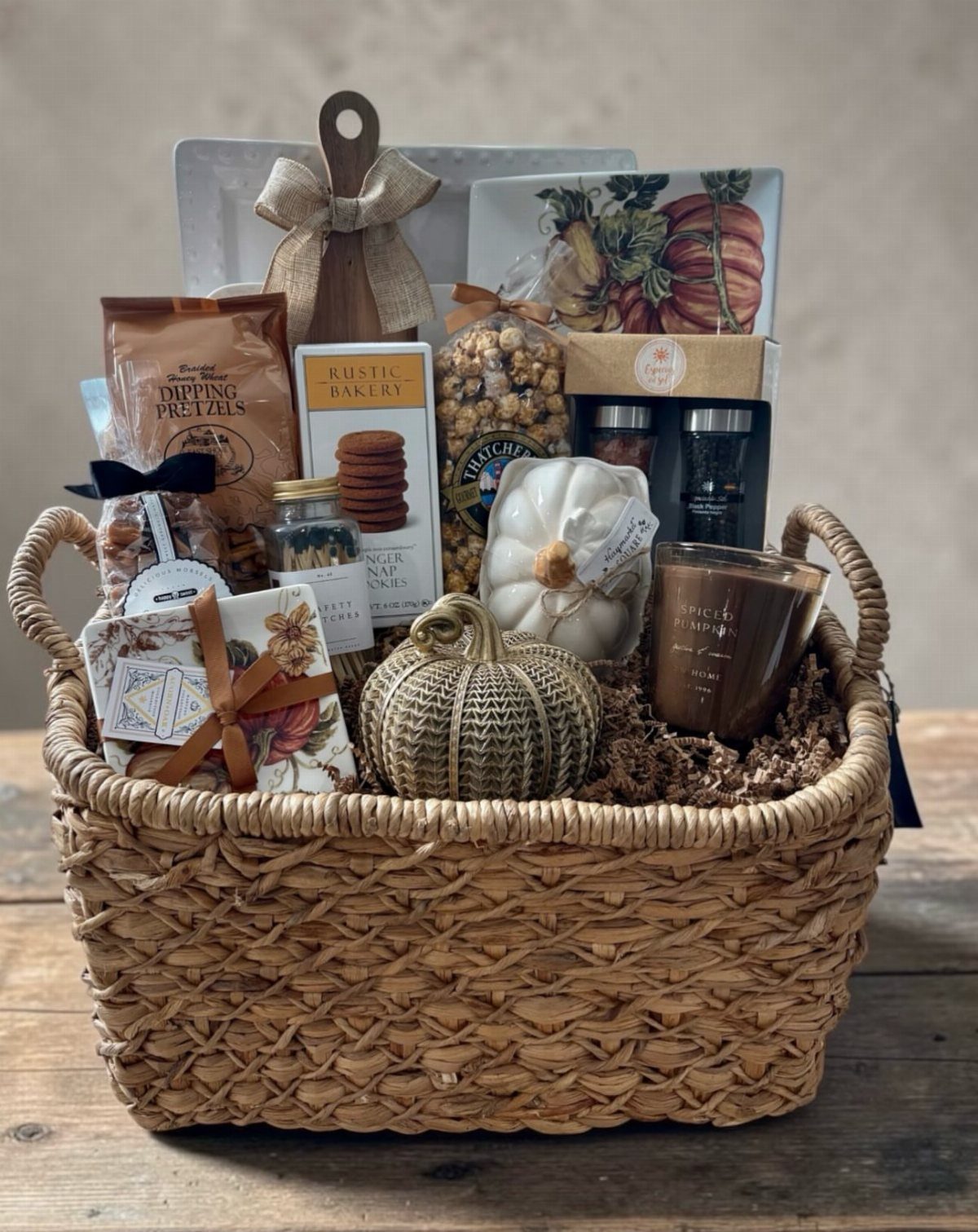 Woven gift basket filled with autumn snacks, decorative pumpkins, and a scented candle.