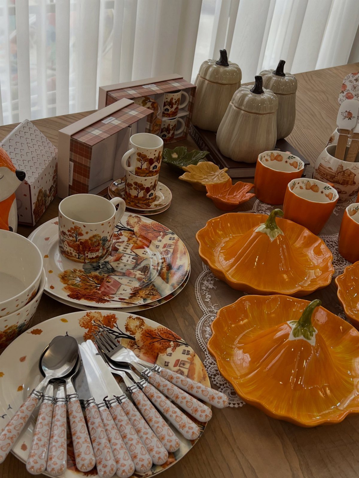 Autumn-themed tableware featuring pumpkin-shaped bowls, patterned plates, and matching mugs on wood.