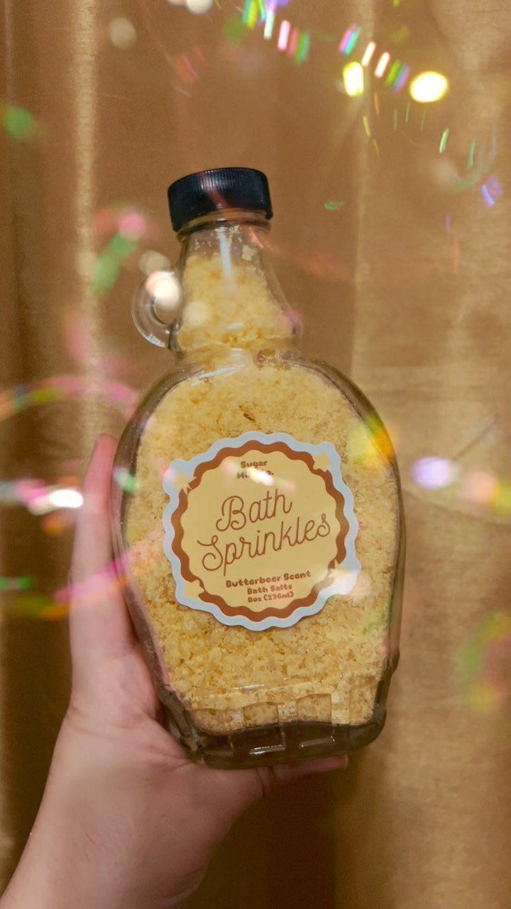 Glass bottle filled with yellow butterscotch scented bath sprinkles held by a hand.
