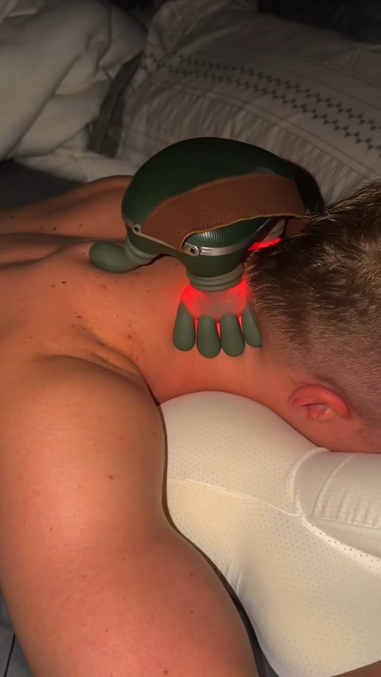 Man lying on a pillow using a green electric neck massager with red light.