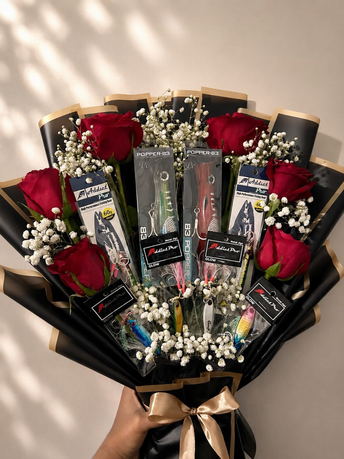 Bouquet of red roses and baby's breath mixed with packaged fishing lures.