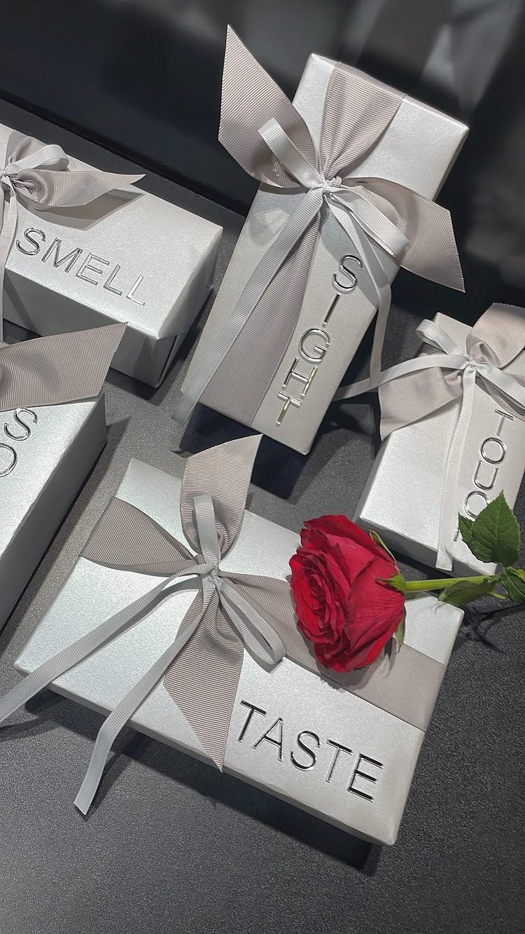 White gift boxes labeled with five senses, tied with ribbons and a red rose.