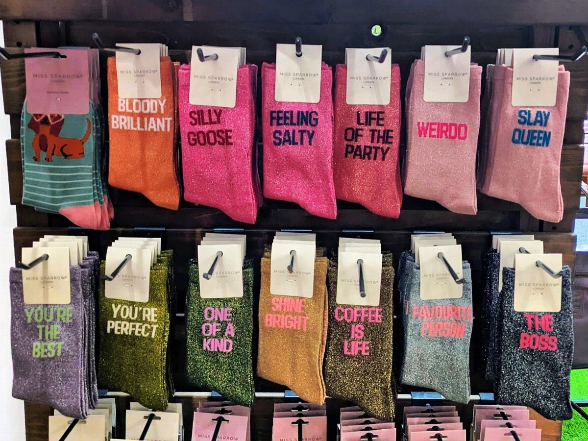 Colorful novelty socks with humorous phrases displayed on a dark wooden retail rack.