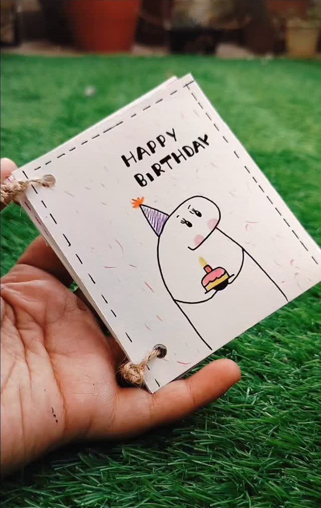 Handmade birthday card with a cute character drawing held over green grass.
