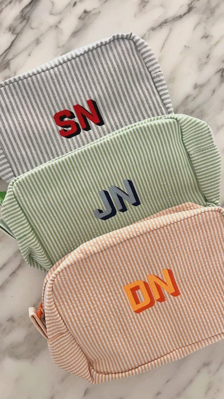 Three corduroy toiletry bags with colorful monogrammed initials on a marble background.