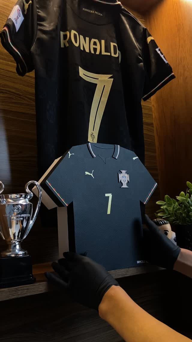 Black soccer jersey with gold number 7 held by gloved hands near trophy.