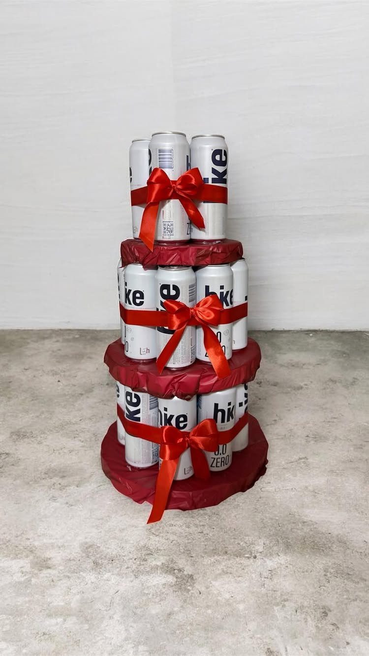 Beer can cake with three tiers wrapped in red ribbons and bows.