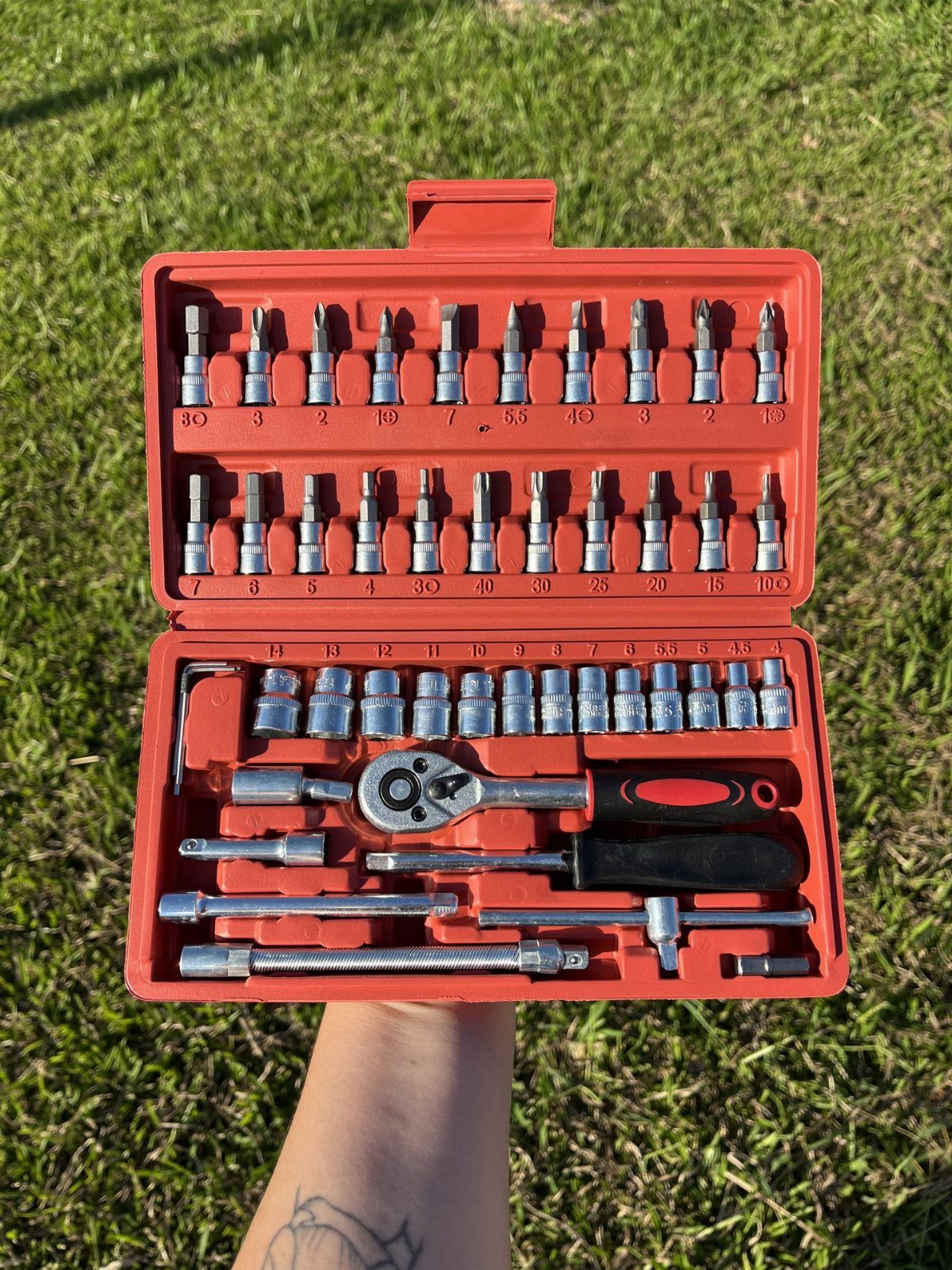 Red tool kit case filled with silver sockets and a ratchet wrench held outdoors.