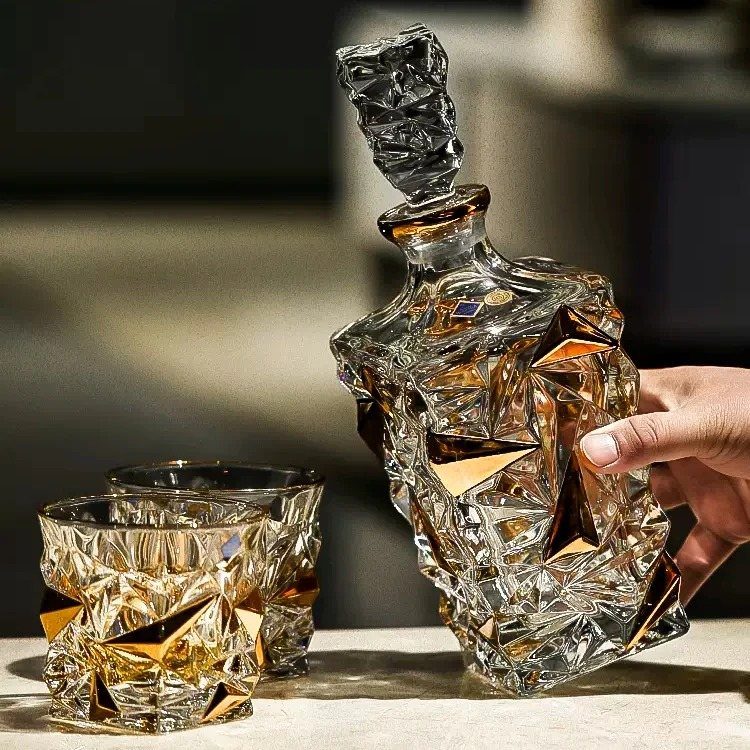 Geometric crystal whiskey decanter and two matching glasses filled with amber liquid.