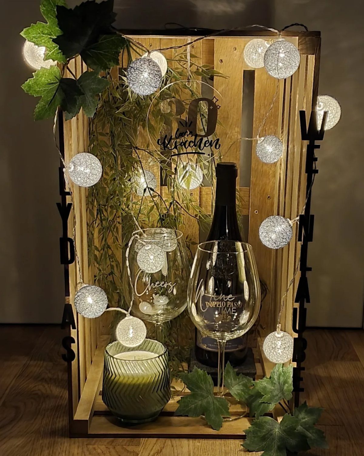 Wine bottle and glasses in a wooden crate with string lights and ivy.