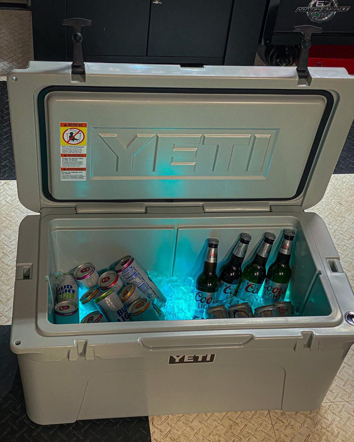 Grey YETI cooler open and filled with ice, beer bottles, and canned drinks.