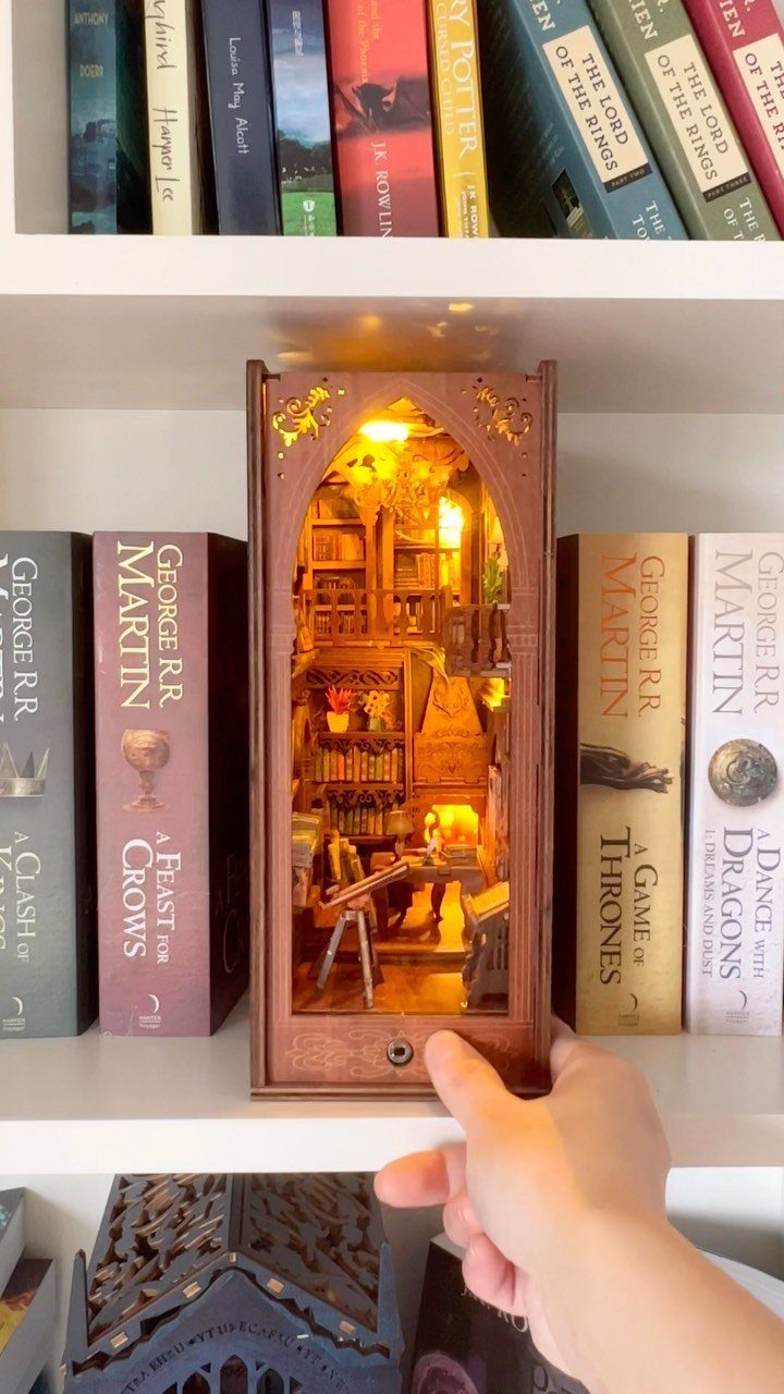 Miniature illuminated library book nook placed between hardcover books on a white shelf.