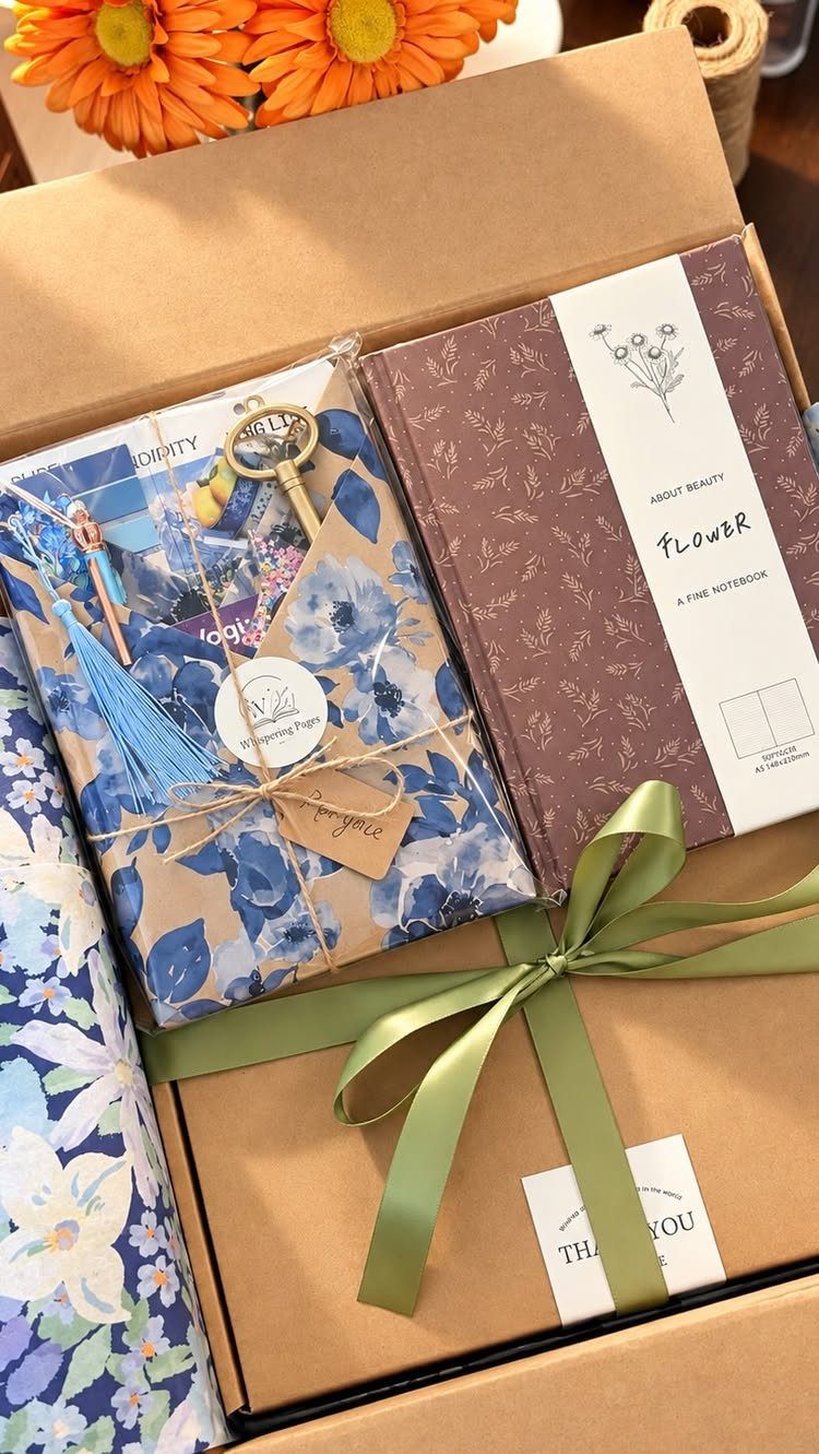 Gift box containing a brown notebook and blue floral wrapped items with green ribbon.