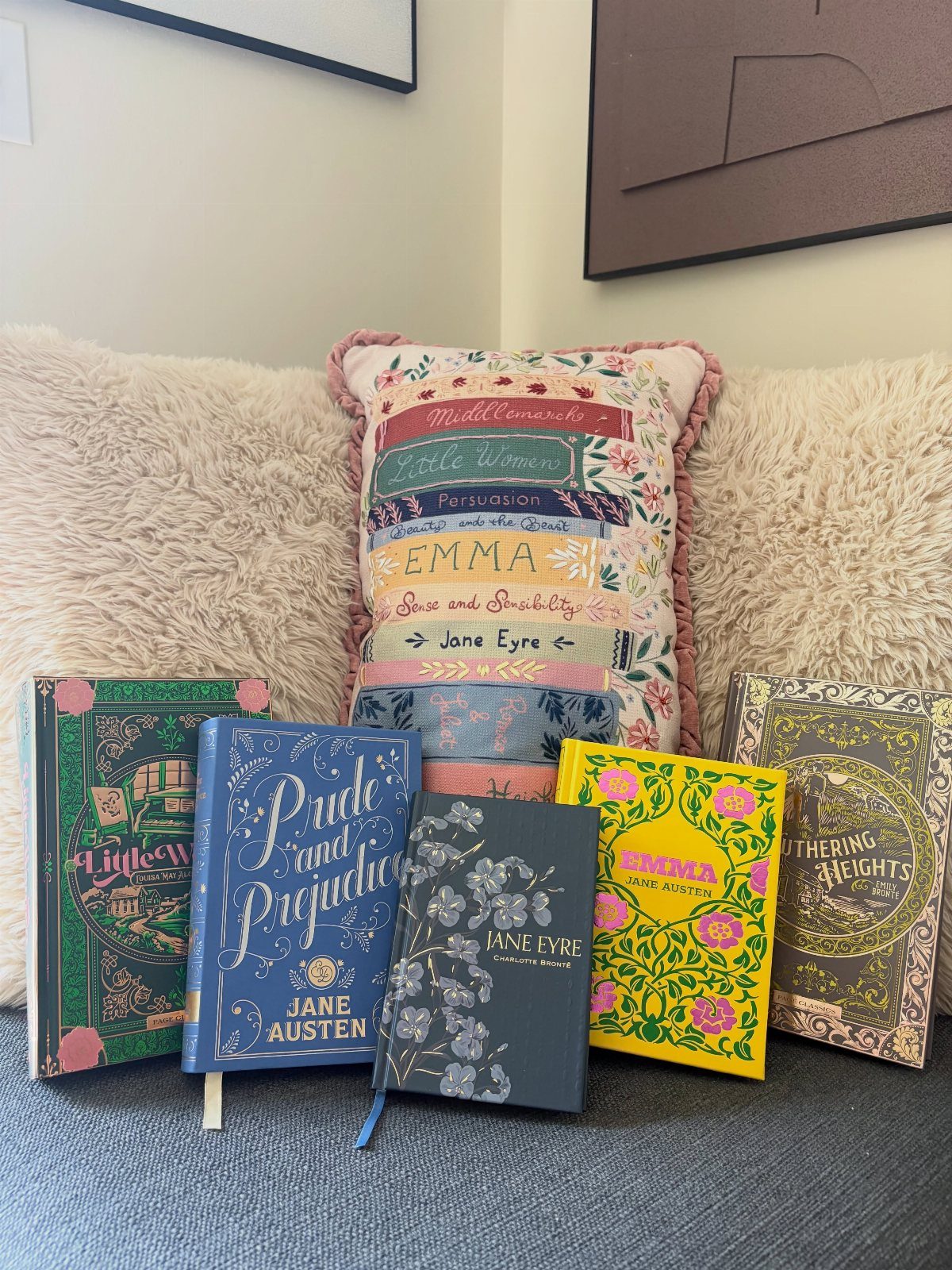 Classic hardcover books and a book-themed throw pillow on a grey sofa.