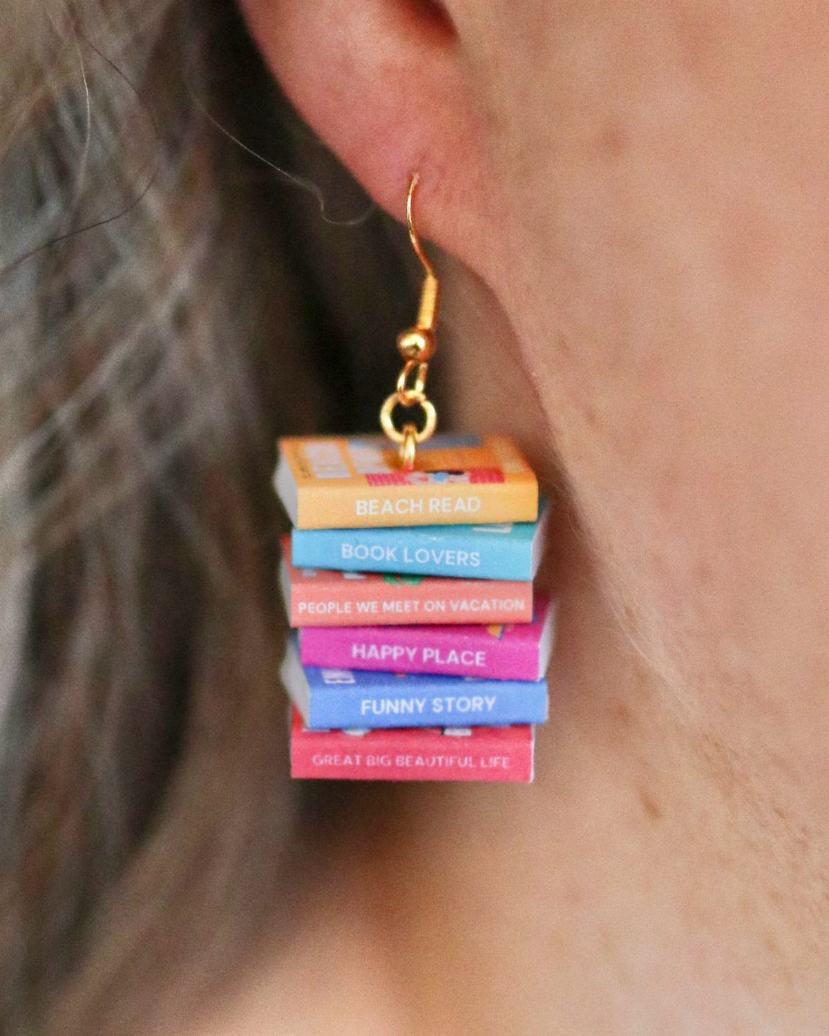 Miniature colorful book stack earring hanging from a person's earlobe.