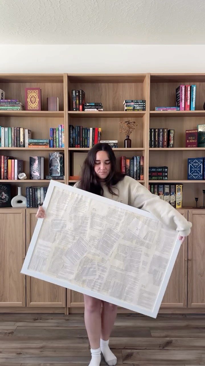 Woman holding a large framed piece of art made from book pages.