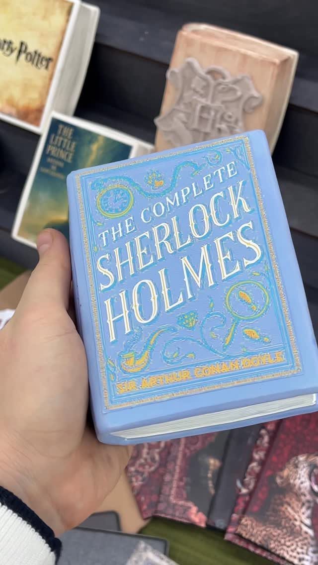 Light blue Sherlock Holmes hardcover book held in a hand among other books.