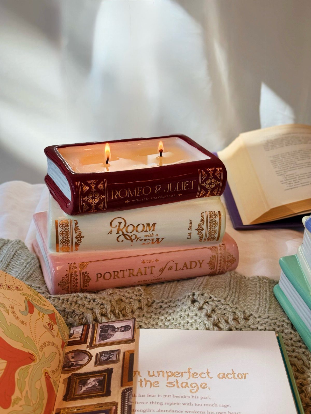 Book-shaped candle titled Romeo and Juliet lit atop a stack of vintage books.