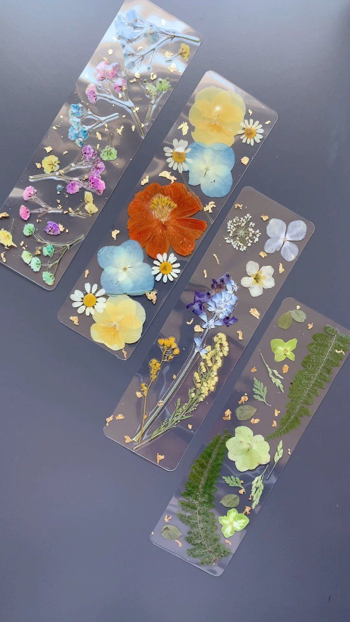 Four transparent resin bookmarks with pressed colorful flowers and gold foil flakes.