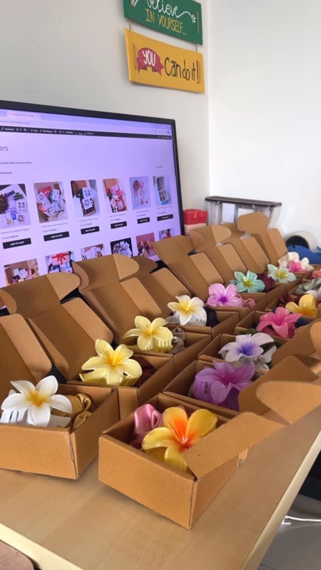 Small brown gift boxes containing colorful artificial plumeria flowers arranged on a table.