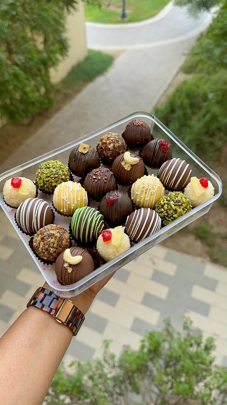 Assorted decorated chocolate truffles in a clear plastic container held by a hand.