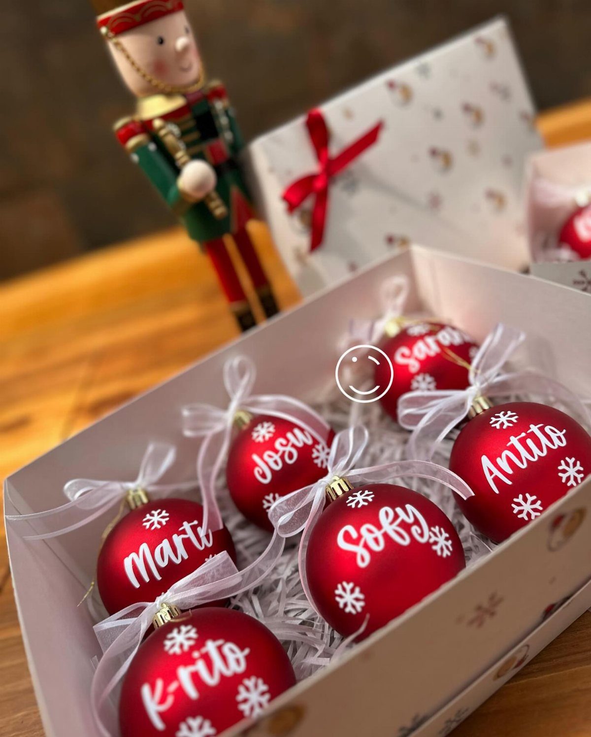 Red personalized Christmas ornaments with white names in a white gift box.