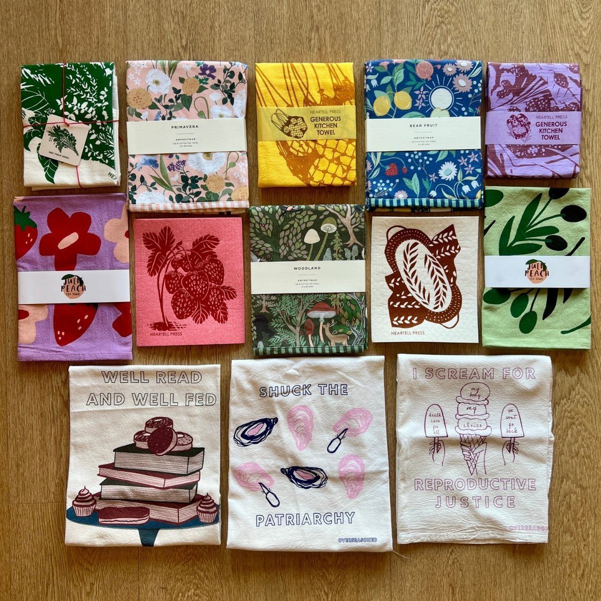 Colorful printed fabric tea towels arranged in rows on a wooden floor.