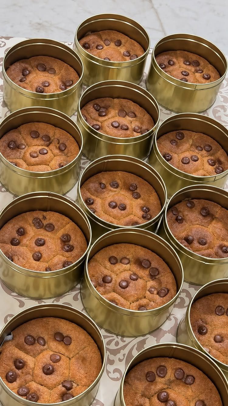 Chocolate chip cookies individually packaged in small gold tins on a patterned cloth.