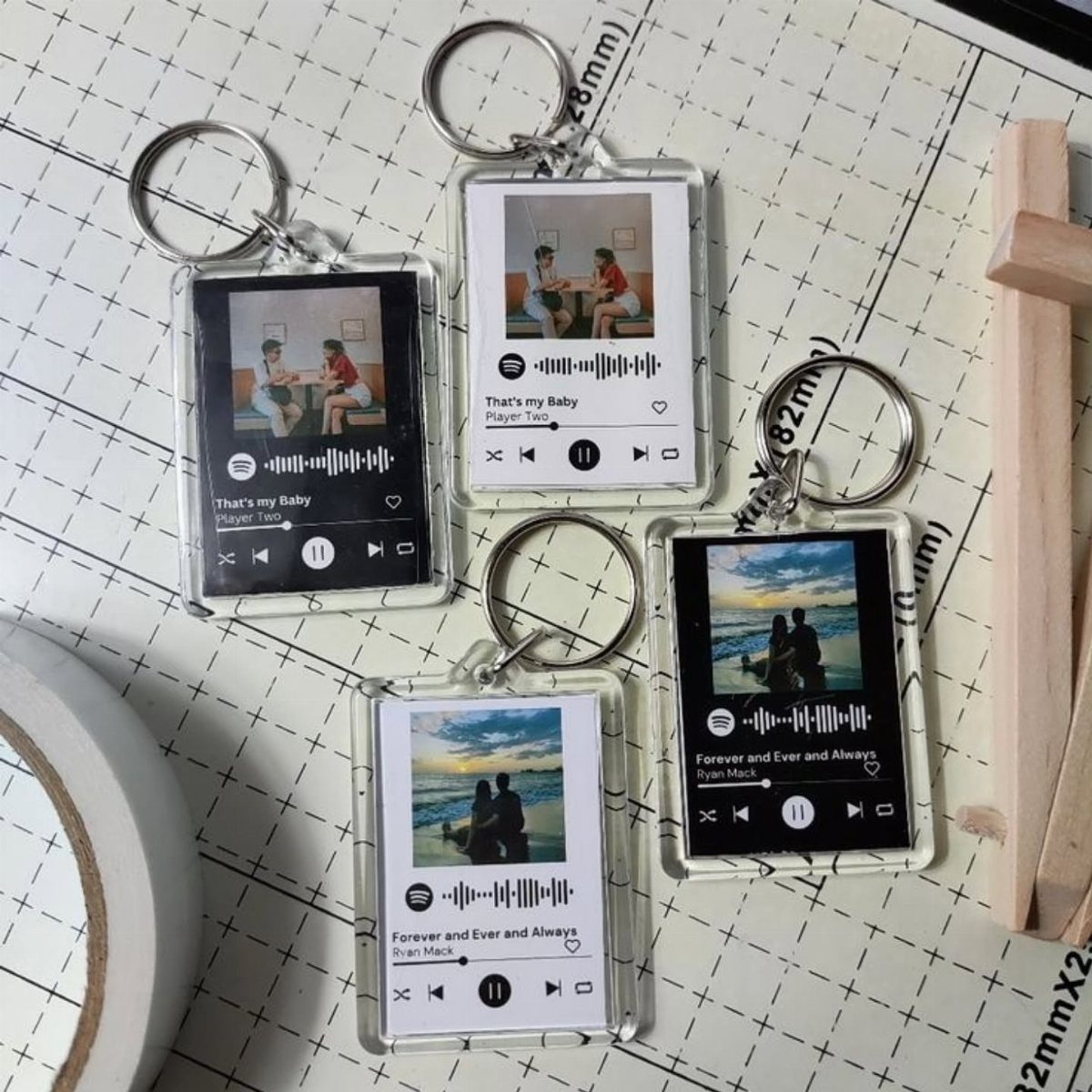 Four acrylic keychains with personalized photos and music player designs on a grid mat.