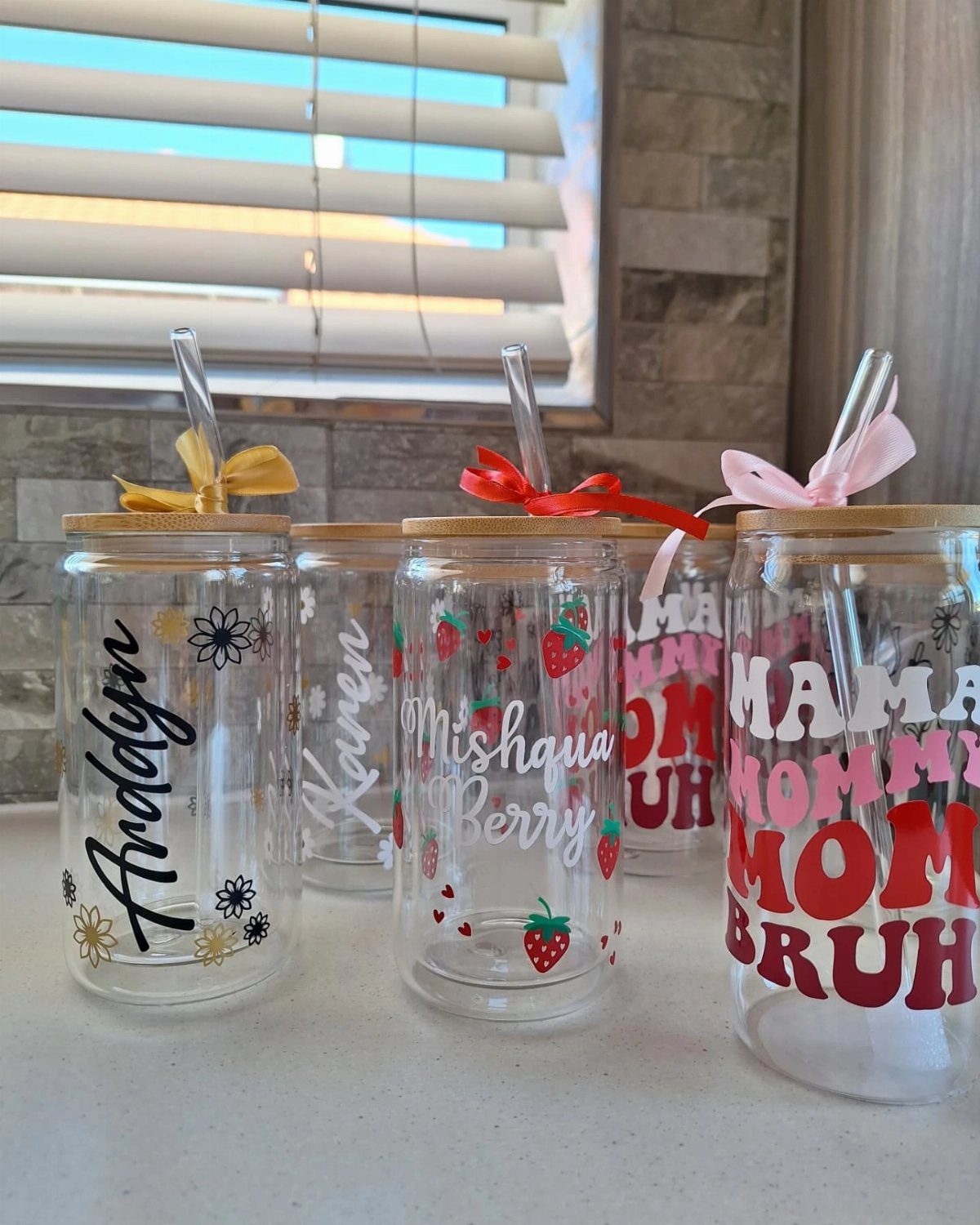 Personalized glass jars with bamboo lids, straws, and colorful ribbons on a counter.