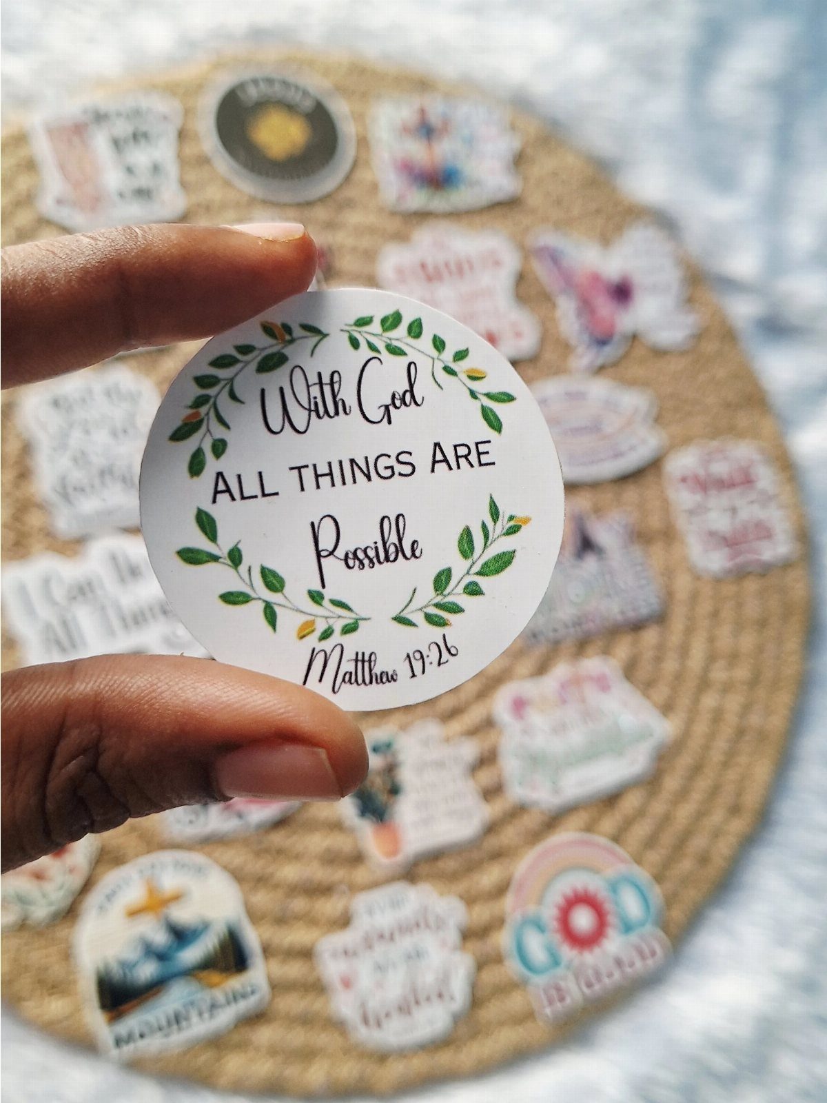 Circular white sticker with Bible verse held over a collection of faith stickers.