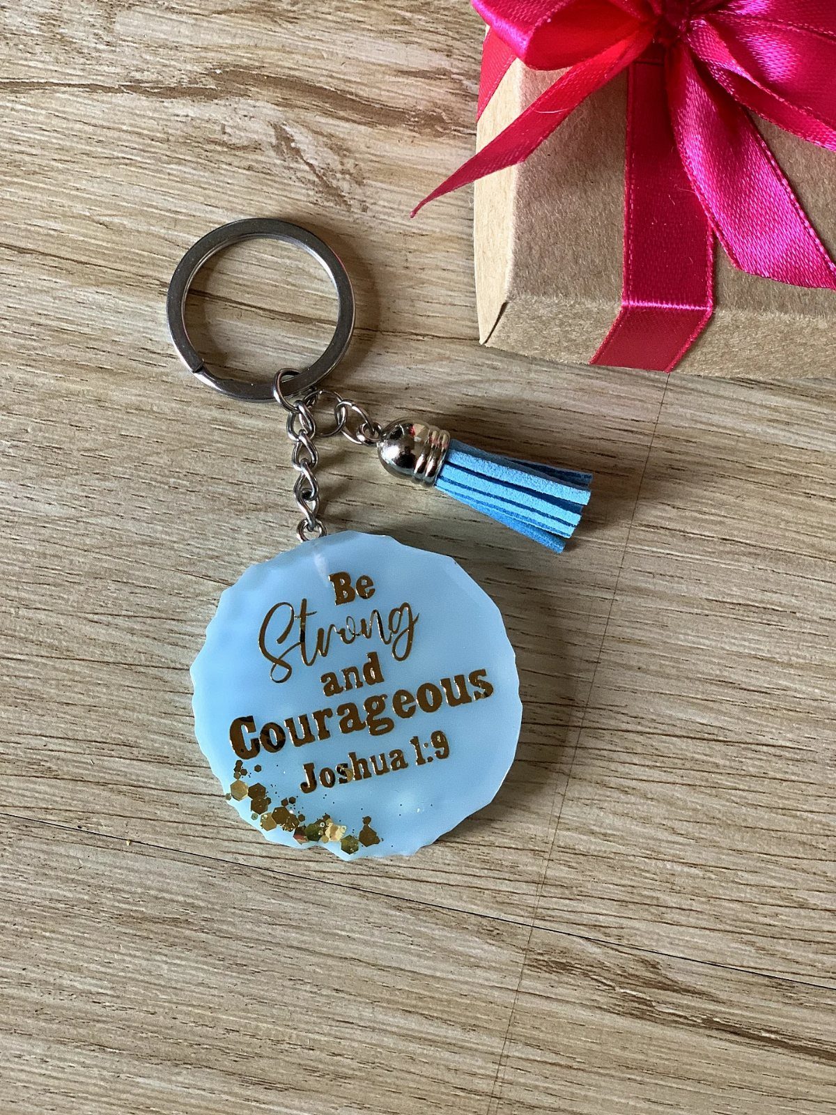 Blue resin keychain with Joshua 1:9 scripture and a blue tassel on wood.