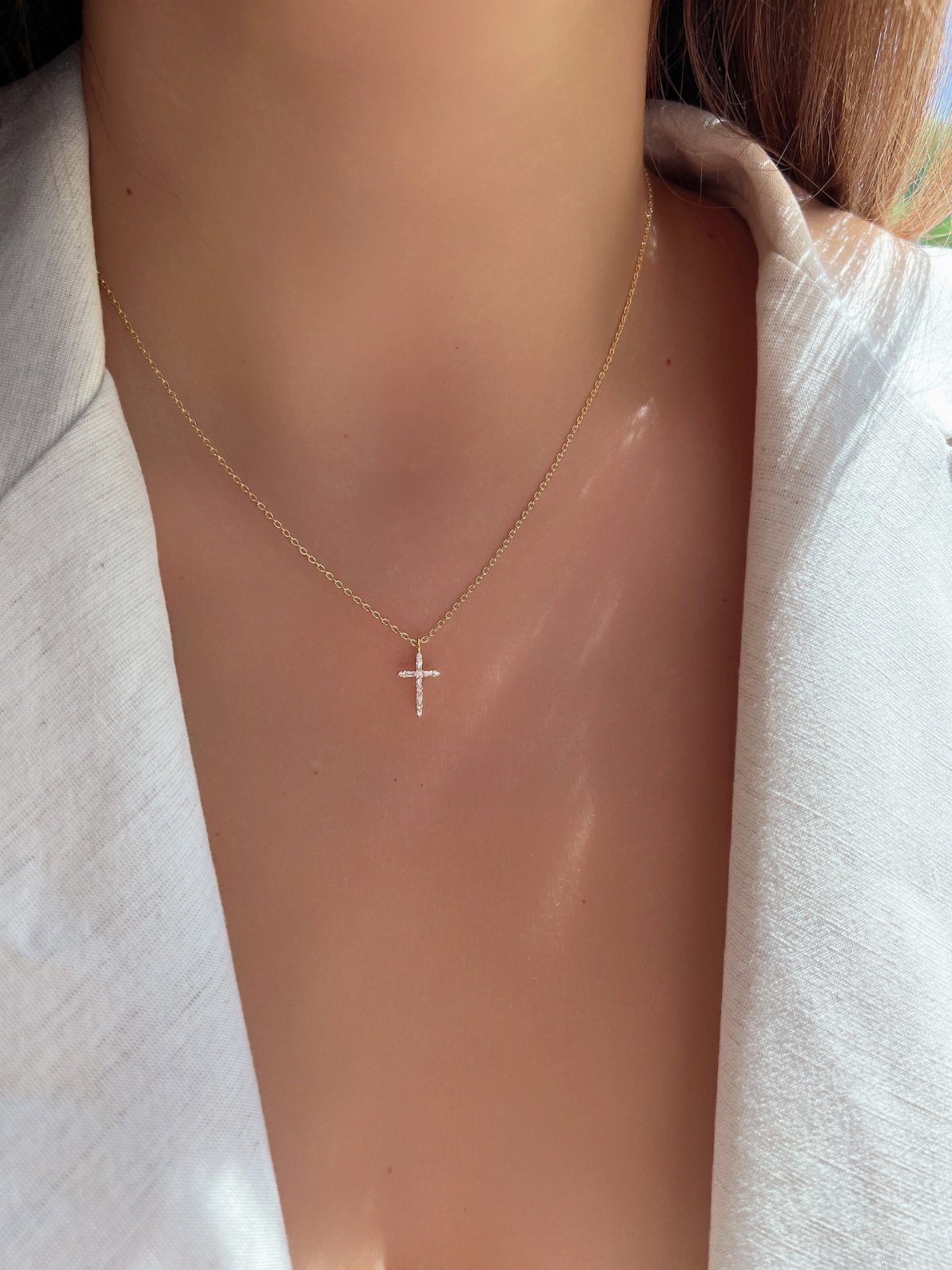 Gold chain necklace with a small sparkling cross pendant worn by a woman