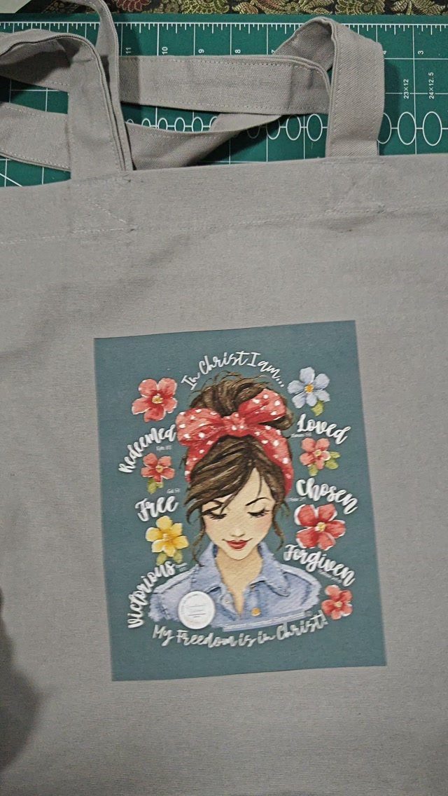 Grey canvas tote bag with a faith-inspired illustration of a woman and flowers