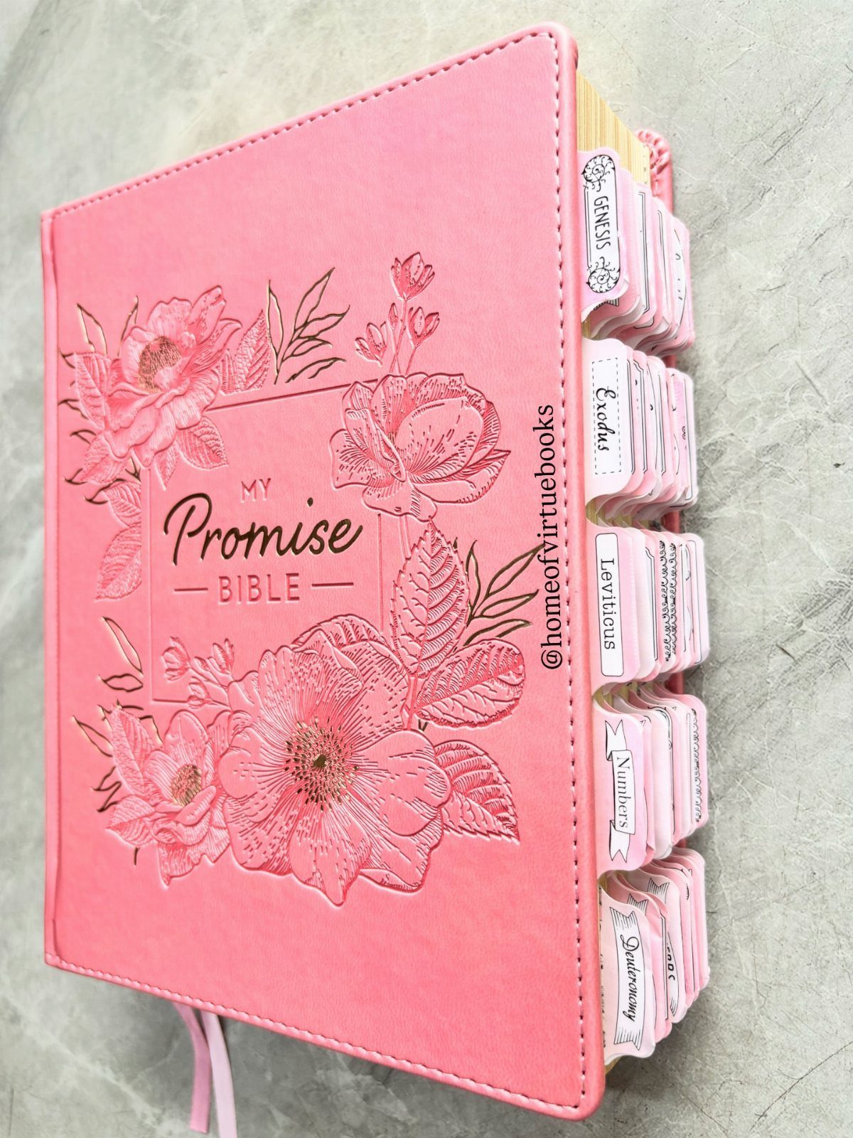 Pink Promise Bible with embossed flowers and white indexed tabs on grey stone.