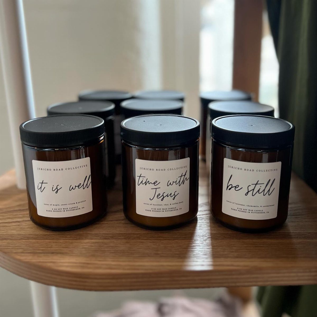 Amber glass candles with faith-based labels on a wooden surface.