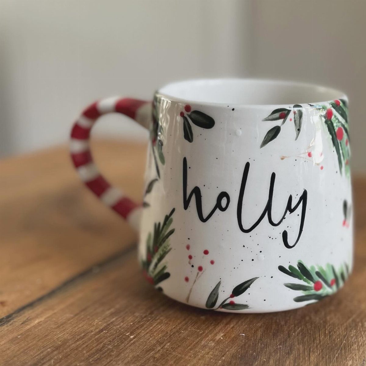 White ceramic mug with red striped handle, name Holly, and festive berry decorations.