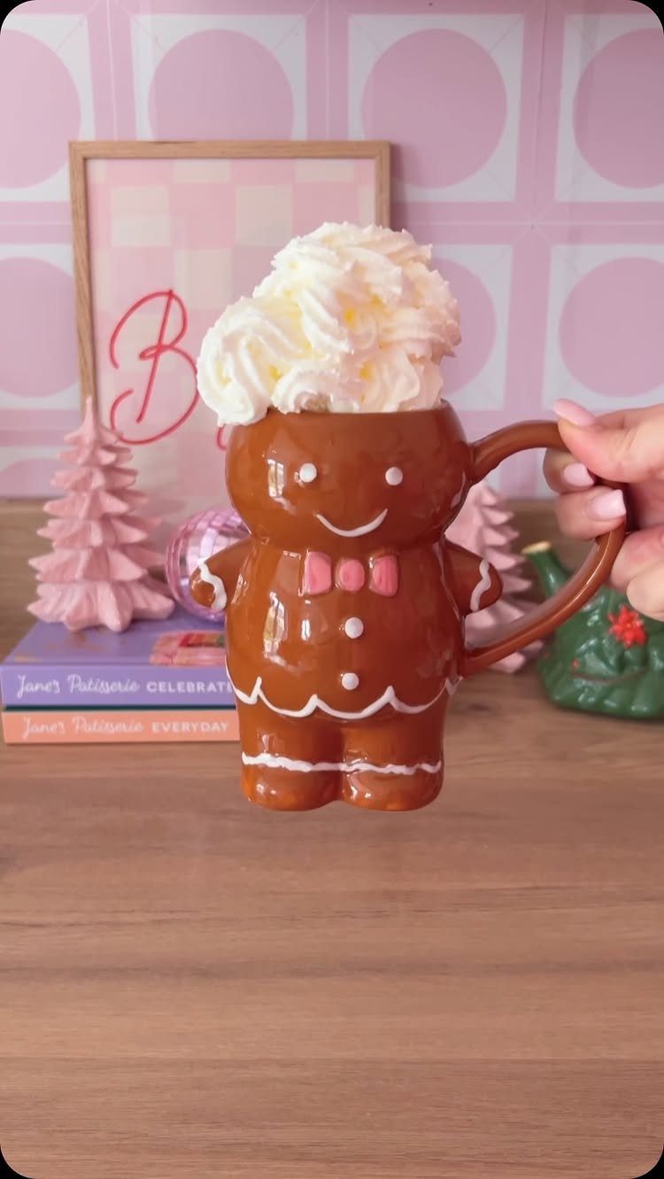 Gingerbread man shaped ceramic mug filled with whipped cream on a wooden table