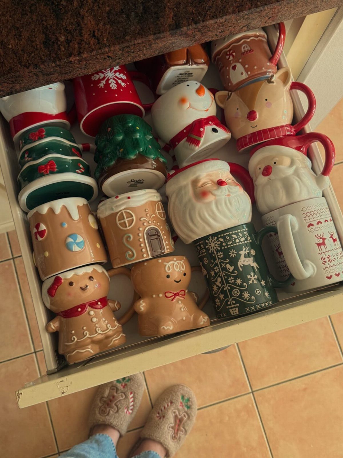 Assorted Christmas ceramic mugs in a drawer, including a green Christmas tree mug.