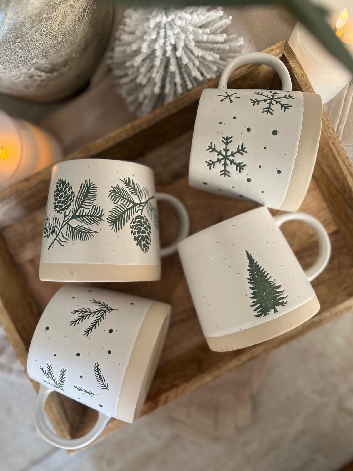Four white ceramic mugs with green winter forest illustrations in a wooden tray.