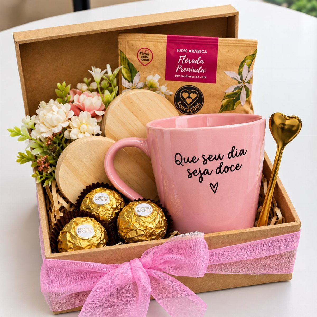 Pink coffee mug gift basket with chocolates, coffee packet, and white flowers.