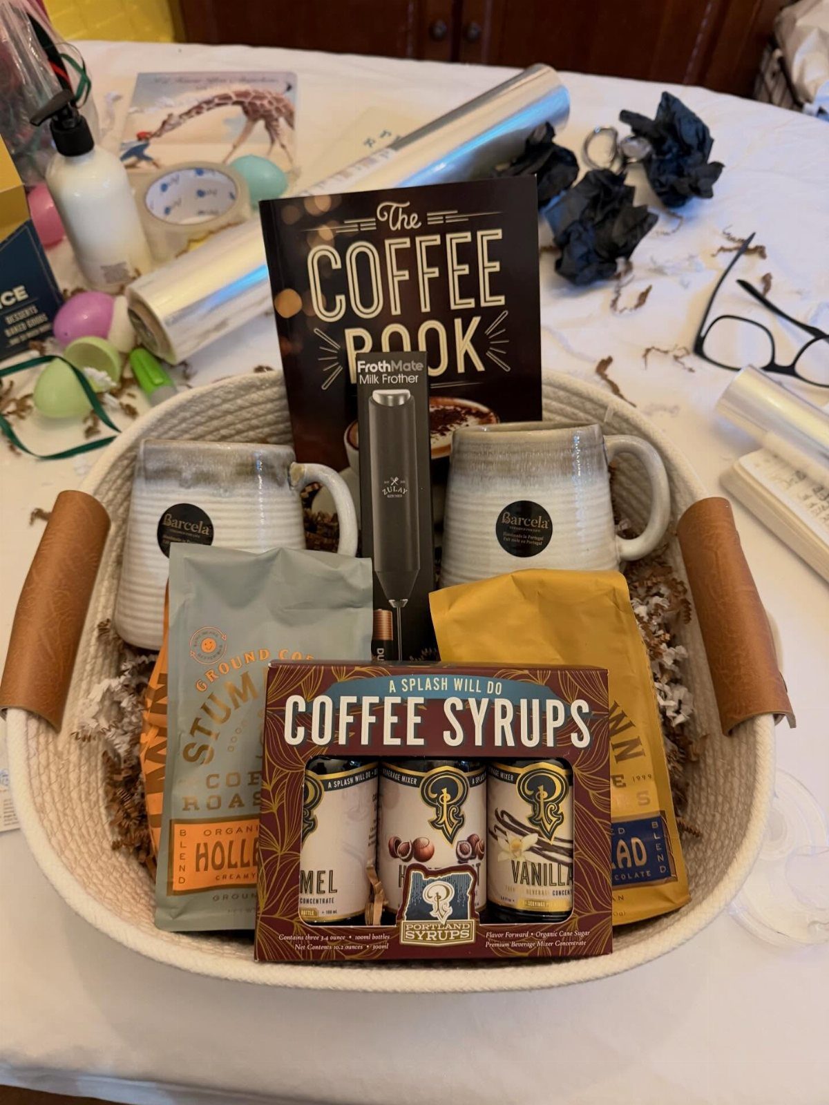 Coffee gift basket with mugs, coffee bags, syrups, and a coffee book.