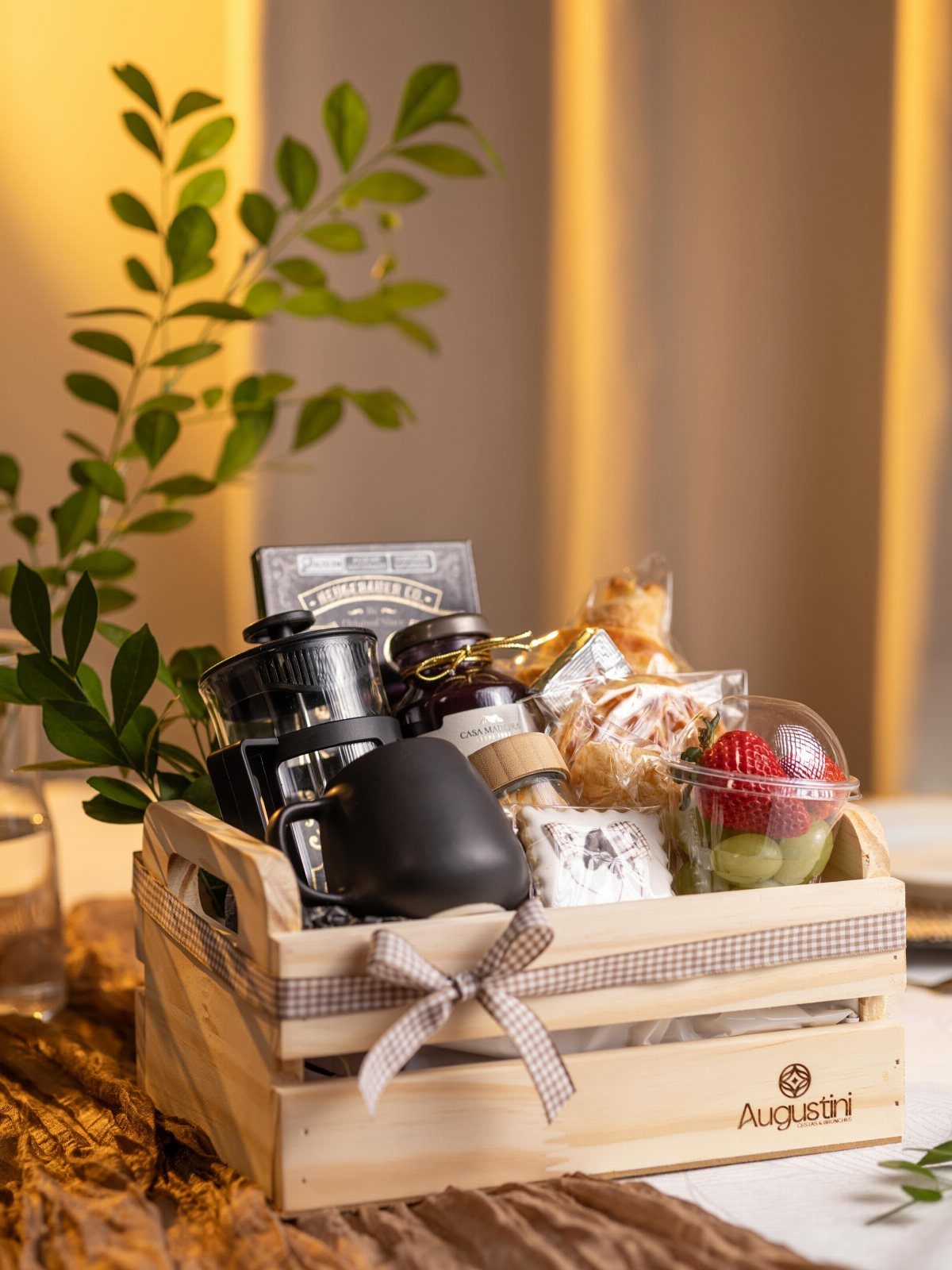 Wooden gift crate with French press, black mug, snacks, and fresh fruit.