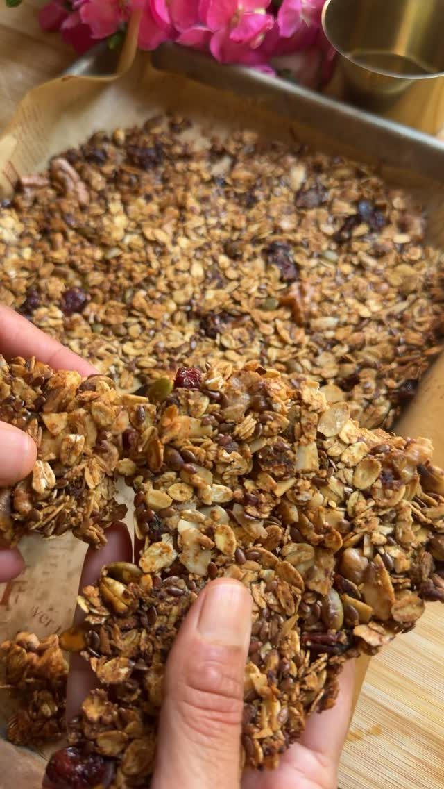 Homemade granola clusters being broken by hand from a parchment-lined baking sheet.