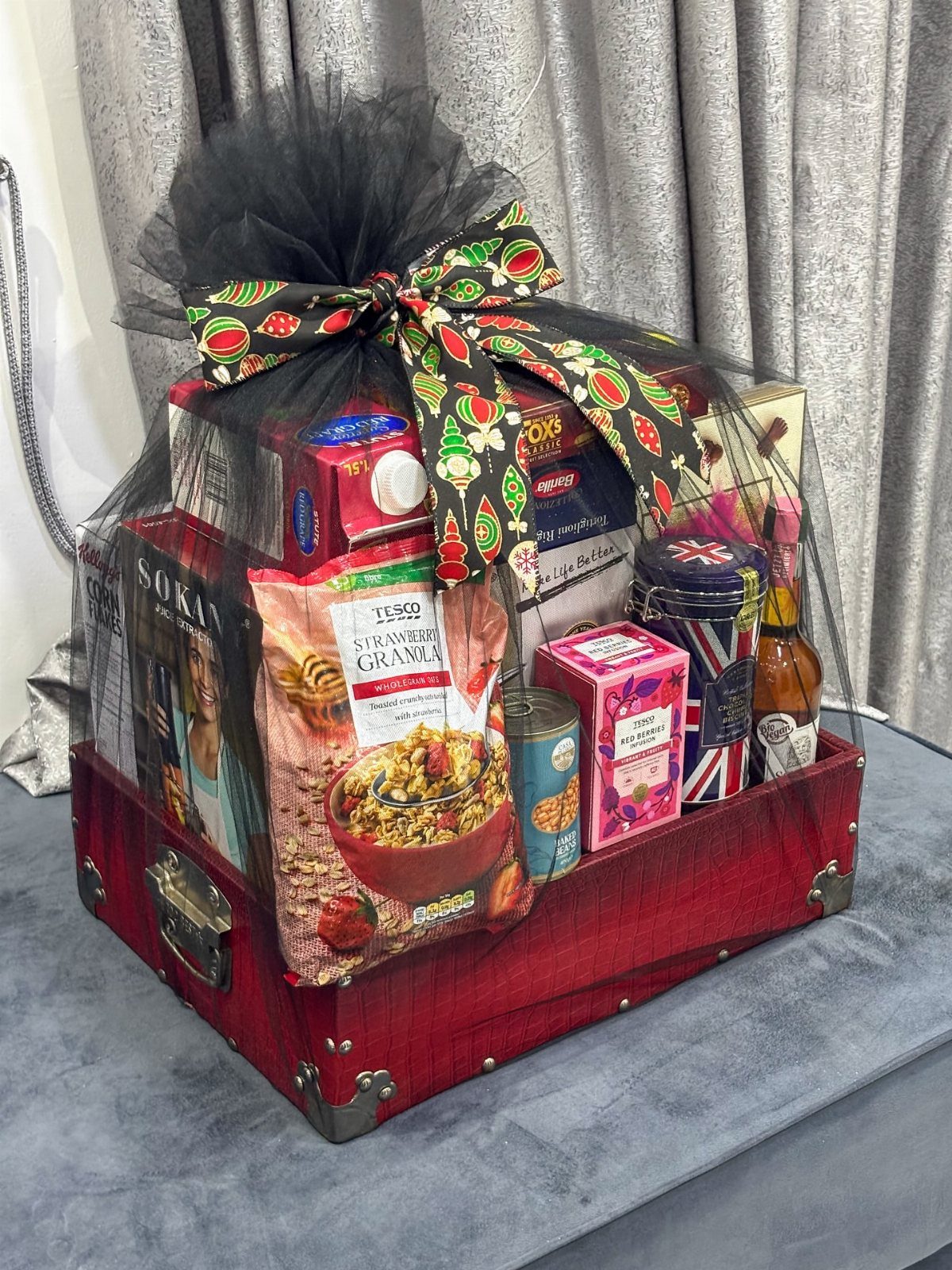 Red suitcase gift basket filled with assorted snacks and treats wrapped in tulle.
