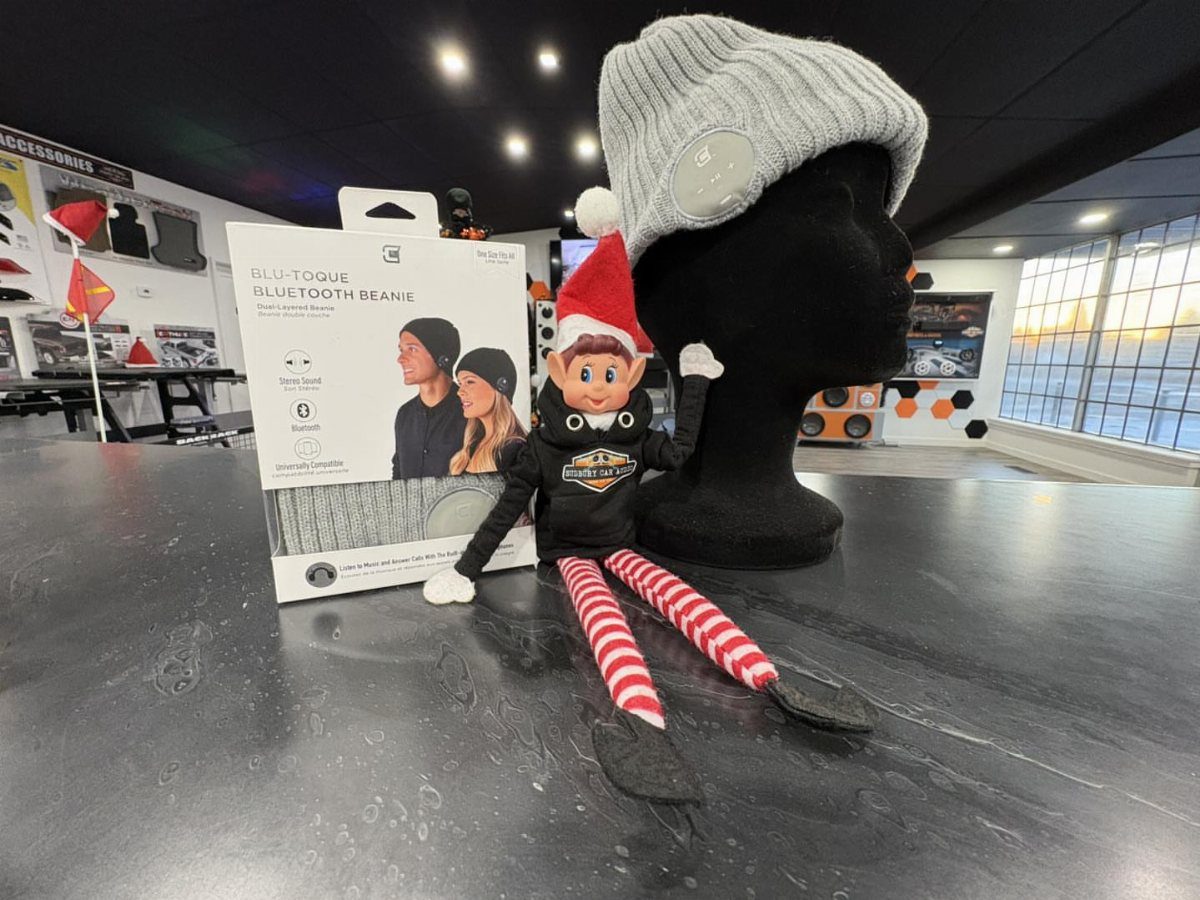 Grey Bluetooth beanie on a mannequin head next to its product packaging and elf doll.